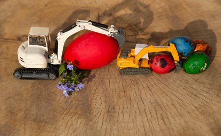 Two models of toy excavators with brightly colored, painted large and small eggs. Easter spring holiday concept for construction companies. Business congratulations postcard. copy spaceの写真素材
