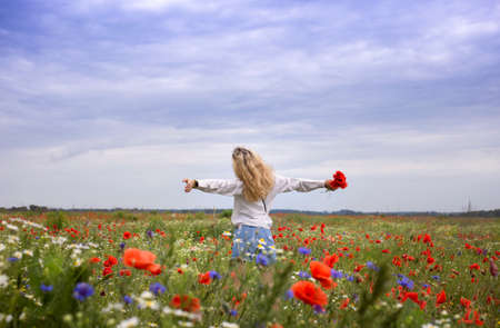 unrecognizable woman with her arms spread apart stands among red poppy flowers in meadow. Hello summer. digital detox, weekend in nature, search for inspiration, enjoy moment. Energy of the earthの写真素材