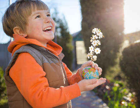 cute laughing boy of 4 years old holds small ball - globe from which spring blossoming apricot branch sticks out in bright backlight. Eco concept, environmental education. Mother's day earthの写真素材