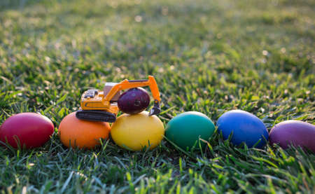 model of a toy excavator, painting in rainbow colors eggs on the grass. Business concept of Easter greetings for construction companies. postcard. copy spaceの写真素材