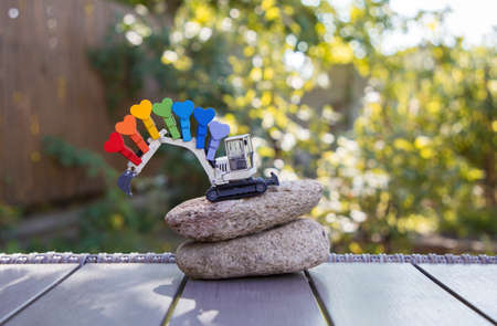 small metal model of toy excavator on two large stones. Bright pins in rainbow colors are pinned to...