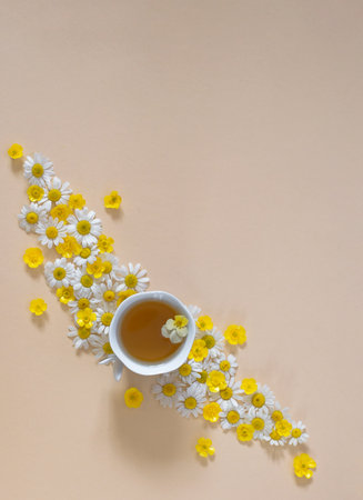 cup of tea among beautifully laid out small flowers of white daisies and yellow buttercups on a beige background. Aromatherapy, natural ingredients, harmony. Good morning. Flower fantasy. Hello summerの写真素材