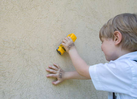 yellow model of a toy school bus in the hands of a little schoolboy in a white shirt drives along a beige wall. Knowledge Day. Back to school conceptの写真素材