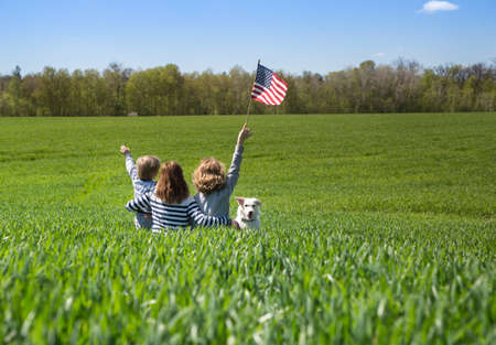 people hug among the green wheat field, back view. Patriotic family with American flag, sunny day, nature. Partiotism, pride, freedomの写真素材