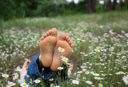 bare feet of a child lying on the ground in a field of daisies in the forest. joy, cheerful positive atmosphere, happy childhood. Hello summer, Energy of nature. Earth dayの写真素材