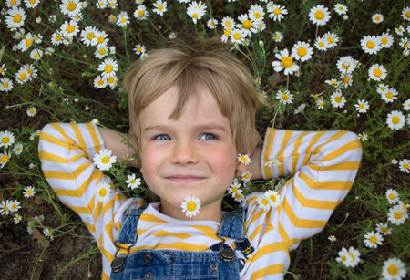 Portrait of a cute smiling toddler boy lying among a chamomile field. Summer mood, childhood dreams,...