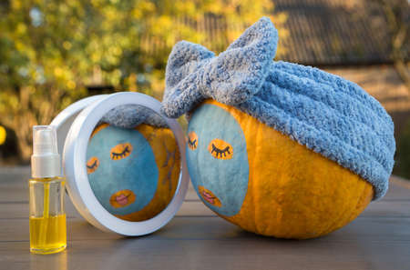 large orange pumpkin with painted eyes, lips and a clay mask in front of a mirror. enjoys beauty treatments. Humor beauty concept. selictive focus. Autumn moodの写真素材