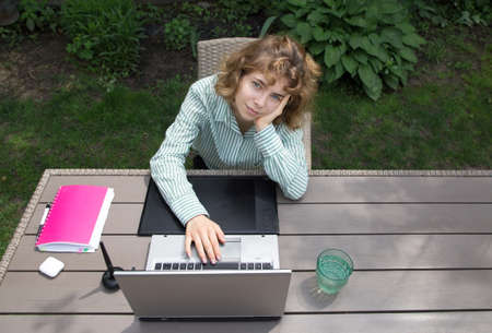 pretty young woman sitting in the garden at the table, working on a laptop, work at home online,...