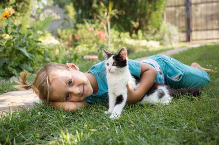 kid plays outdoors in the summer with his beloved black and white kitten. the child is friendly with the pet. Toddler boy lies on the grass with the cat. Holidays in pleasure, joy, positiveの写真素材