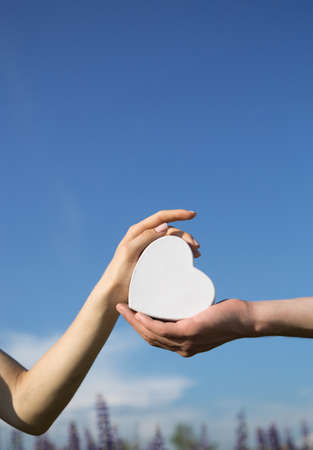 concept of love, support, hope, health care. male and female hands holding a white heart on a background of blue sky. World heart day. Copy spaceの写真素材