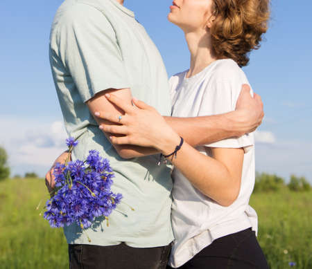 unrecognizable young couple in love, rest and hug in nature on a sunny day. young boy and girl with a bouquet of cornflowers. tender feelings, romance, freedom, tenderness for each other. love conceptの写真素材