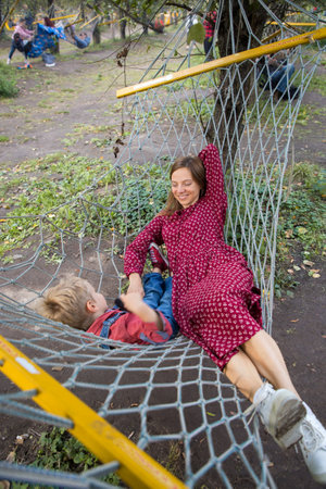 Smiling woman and little boy relaxing together in a hammock. Mother and son are resting in the park at the weekend outdoors. Family outdoor activities, adventure and pastimeの写真素材