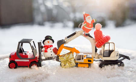 Composition of a model of toy excavators and a warehouse loader, a snowman, Santa in snow. concept for christmas business greetings, new year holidays in construction companies. sun exposureの写真素材