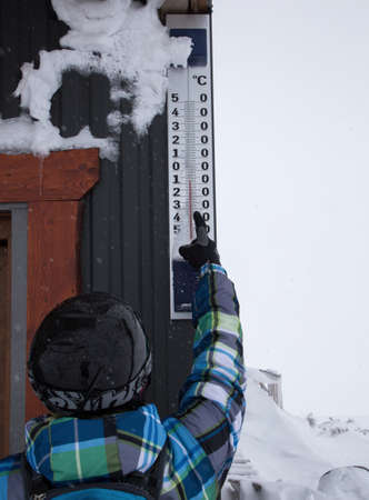 ski resort, a man skier in a helmet points to a large outdoor thermometer. On a scale of minus 8...