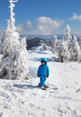 toddler boy in helmet, goggles and blue overalls skiing in beautiful snowy mountains. Winter active entertainment for children. Skiing lesson at an alpine school. Cold, sunny, beautifulの写真素材