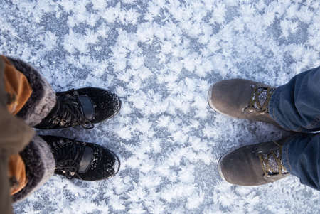 Love Winter. 2 pairs of feet in winter boots stand on the ice on icy colors created by nature itself. Rest in the winter season, an active lifestyle. Cold season. Copy space for text, top viewの写真素材
