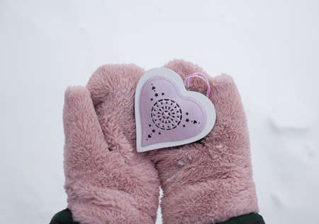 Women's hands in fluffy pink mittens hold a souvenir heart against a background of snow. Love Winter. A symbol of love for a loved one. Surprise for Valentine's Dayの写真素材