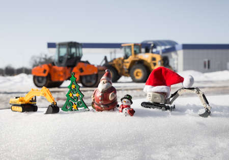composition of small toy excavators, souvenir snowman, santa claus in a row against the background...