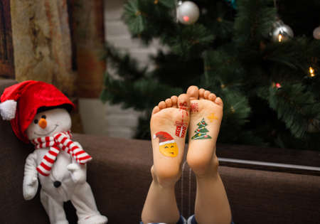 toy snowman and children's bare feet with drawn pictures on the theme of the new year. Christmas celebration concept. positive festive cozy christmas atmosphereの写真素材