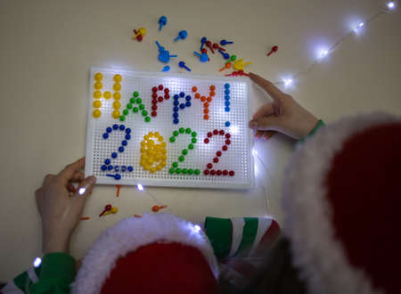 numbers of new year 2022 are lined with plastic colored mosaic. Made by kids in santa hats. Ideas...