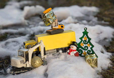 toy excavators, a yellow wagon, a souvenir snowman, golden gifts stand in snow. concept of christmas business funny greetings in construction companies. Selective focusの写真素材