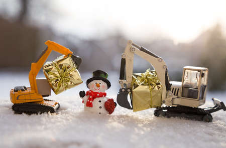 toy excavators, souvenir snowman, gifts in gold paper. preparation for the holiday new year, winter festive mood. concept for Christmas business greetings in construction companiesの写真素材