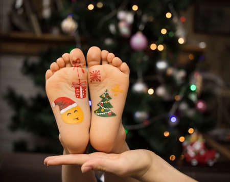 two children's bare feet with painted holiday pictures on the New Year theme. Christmas preparation concept. positive festive cozy christmas atmosphereの写真素材