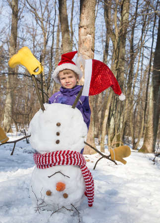 child boy in Santa hat and homemade funny snowman standing upside down on his head. Christmas festive season in a snowy forest. Winter walks and fun with snow. fun, childish joyの写真素材