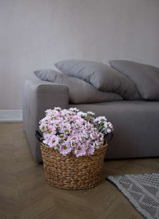 Real photo of the interior with a gray sofa. Cozy living room, natural textures. wicker basket with pink flowersの写真素材