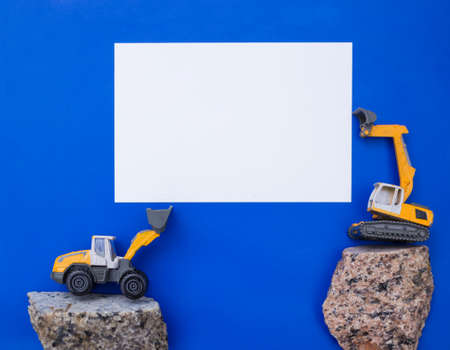 white blank paper for advertising lettering between small toy construction excavator and loader. business - congratulations, day of the builder. Advertising for the construction businessの写真素材