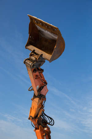 orange arrow with excavator bucket against the blue sky. Road repair works, construction, earthworks, loading, industry. Rental, leasing of construction equipmentの写真素材