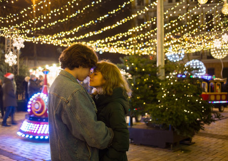 winter vacation, happy young couple in love meets at the christmas market in the evening. There are...