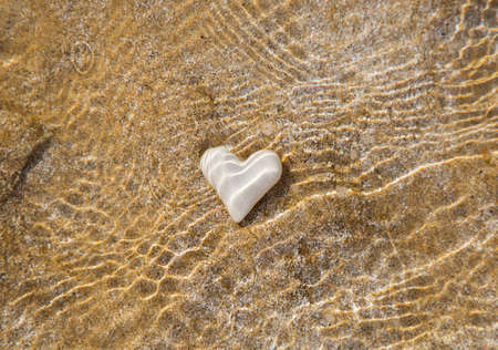 White heart underwater on a sandy beach. Beautiful sun glare. Hello summer, sunshine, vacation, travel, love, romance, recognition of feelings, surpriseの写真素材