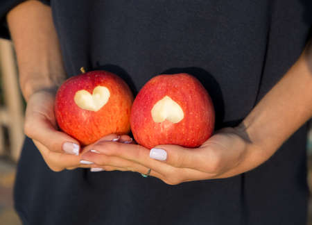 female hands hold two large red apples with hearts carved on them. Delicious harvest, healthy diet food, vitamins, organic apples. surprise for a loved oneの写真素材