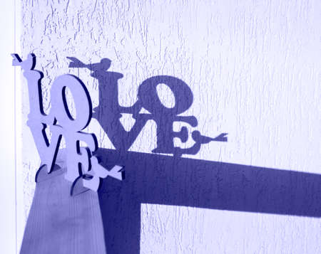 On background of wall there is inscription of word Love, behind it there is a contrasting shadow from letters. Love day concept. tinted in color of year 2022 very peri. Valentine's dayの写真素材