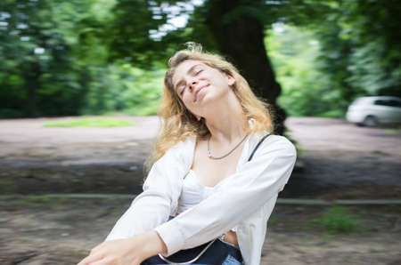 Cute young woman with dreamy happy expression on face relaxing in park on swing. Peace of mind, positive moment in life, joy, satisfaction, carefree day, good mood. Blurred background, selective focusの写真素材