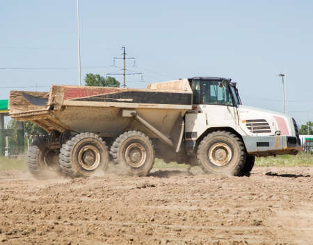 articulated dump truck in motion, driving along a dusty road. Construction machine in the process of...