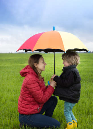 Happy woman and child opposite each other under one bright umbrella having fun outdoors. Spring cloudy weather. Hi spring. Bright and interesting childhood. Active walks of son with his motherの写真素材