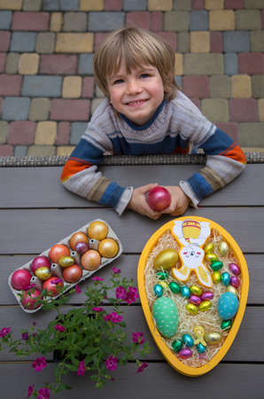 Happy preschool boy stands near the table with Easter decor. colorful chicken, quail and chocolate...