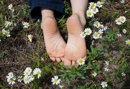 bare feet of a child lying on the ground in a field of daisies in the forest. summer joy, positive...