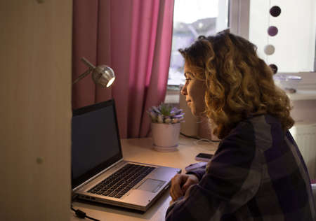 teenage girl of 16-17 years old, student, high school schoolgirl sits at a laptop at a table by...