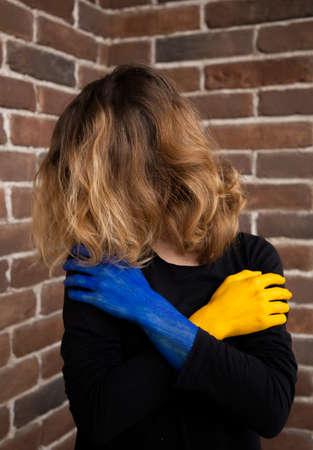 unrecognizable woman, face covered by hair, exhaustedly holding her hands in front of her, painted in colors of the Ukrainian flag. war in Ukraine. suffering of civilians, request for helpの写真素材
