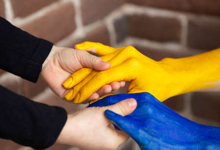 children's small hands hold female hands painted in yellow and blue colors of Ukrainian flag. Family together, peace, care. Support Ukrainians during the war on territory of Ukraine. selective focusの写真素材