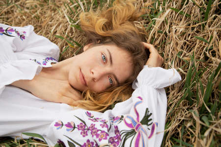 beautiful girl 17-19 years old in an embroidered Ukrainian traditional shirt lies in dry grass. view from above. I am Ukrainian. Stand with Ukraineの写真素材