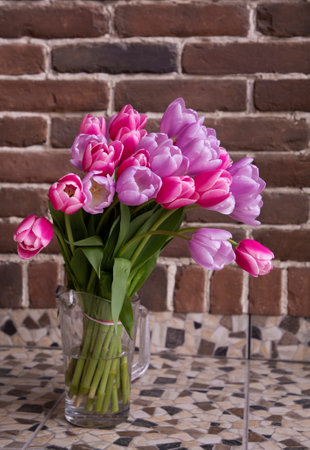 bouquet of pink and lilac tulip flowers on brick wall background with copy space. mother's day gift concept, surprise with love. Festive spring moodの写真素材