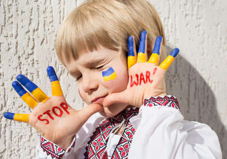 face of frightened boy in national Ukrainian clothes, holds hands in front of him with inscription STOP WAR, his fingers are painted in yellow and blue. Russia's invasion, Children against war.の写真素材