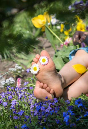 bare feet of a child sitting among flowers. Two daisy flowers between fingers. joy, rest, pampering, positive, happy childhood. Hello summer, energy of nature. earth day. selective focusの写真素材