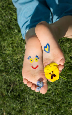 smiling face and heart are painted on children's bare feet in yellow and blue. Children against war. positive atmosphere, hello summer. attracting attention of the world community to the problem of Ukraineの写真素材