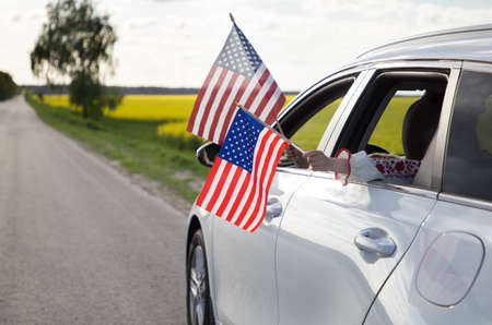 Two American flags hanging out of the window of a white car. United States Independence Day July...