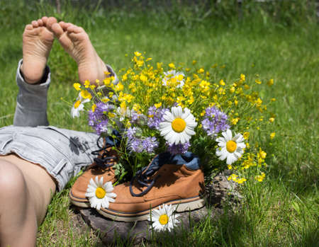 bare feet of child lying on grass, next to bouquet of field flowers in boots. joy, positive atmosphere, happy childhood. hello summer. surprise gift for mom. Active lifestyle, walking. earth dayの写真素材